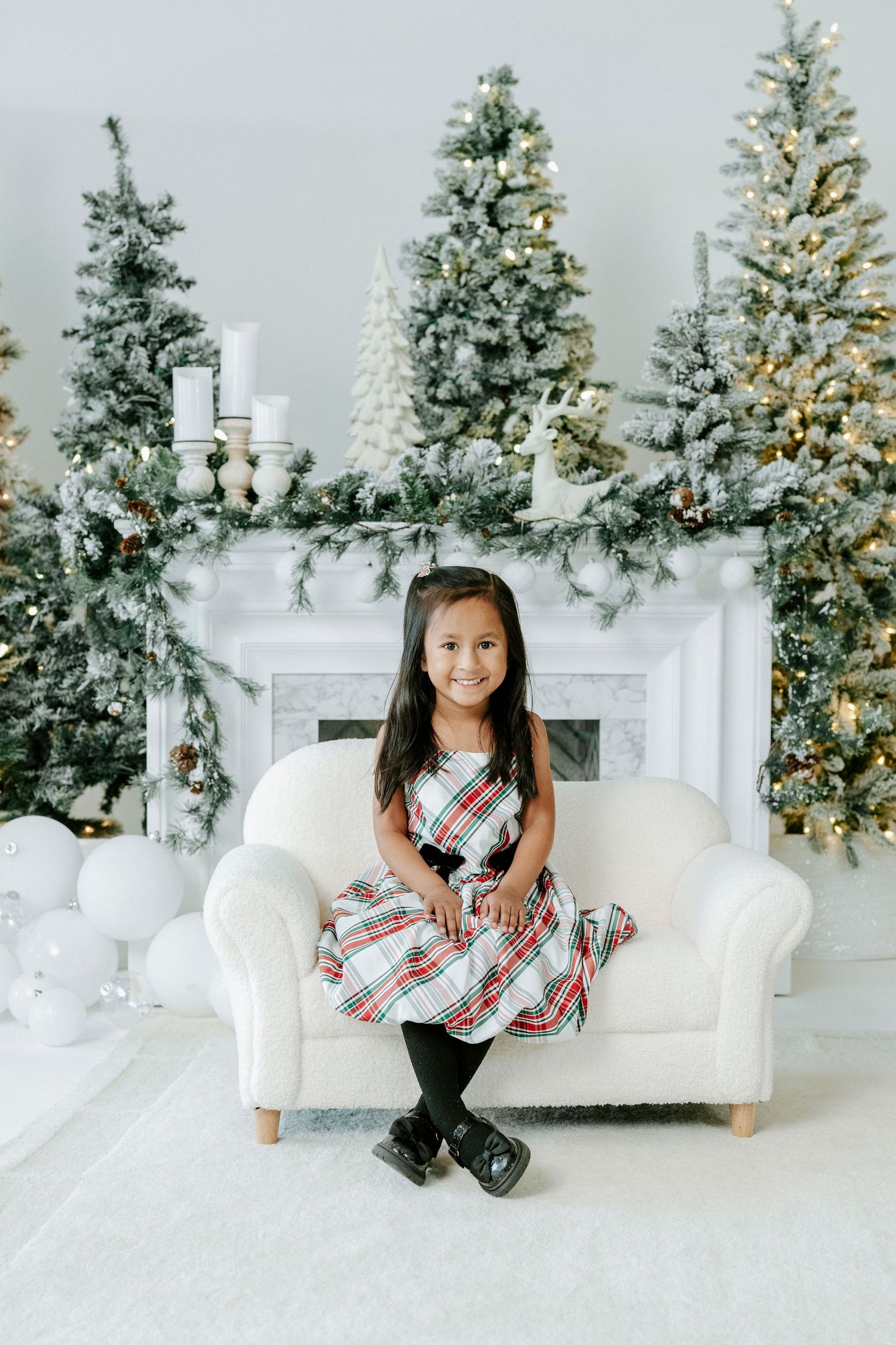 Festive holiday scene with decorated Christmas trees, white fireplace mantle, and cozy white armchair in winter wonderland setting.
