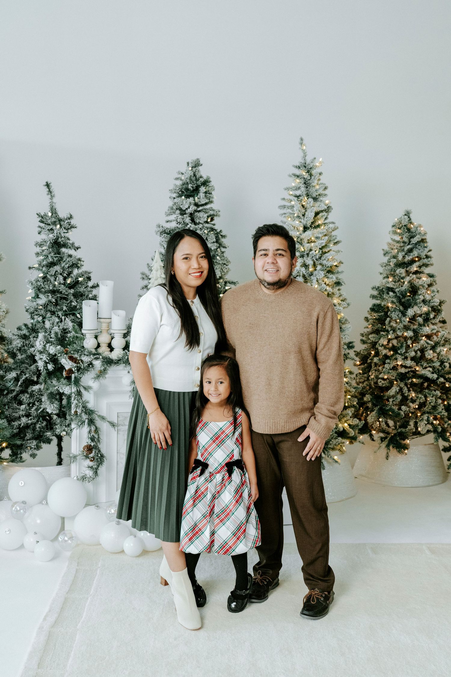 A family poses together in front of decorated Christmas trees and white winter decor in a studio setting.