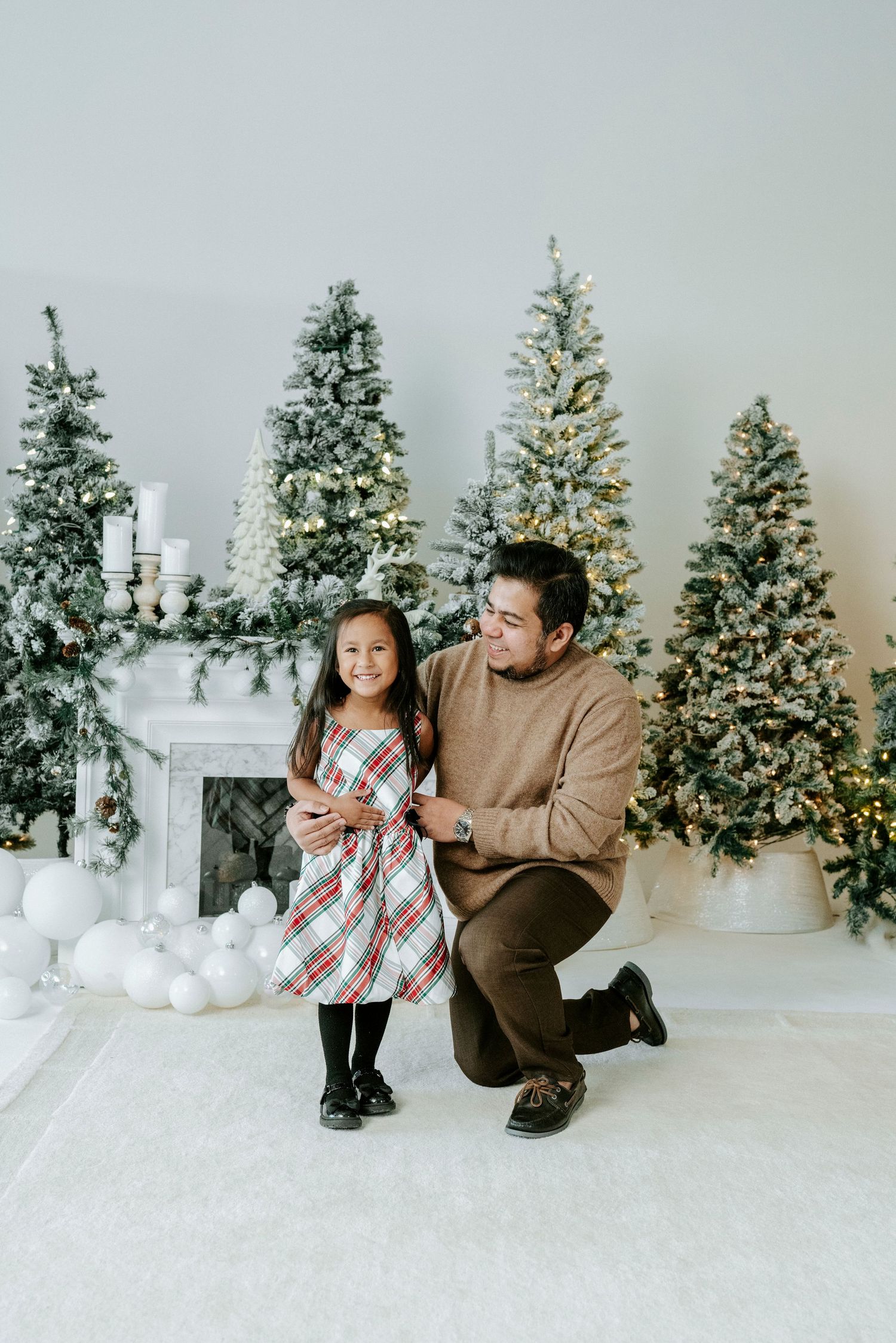 A heartwarming holiday photo session with playful poses in front of lit Christmas trees and white decorations.