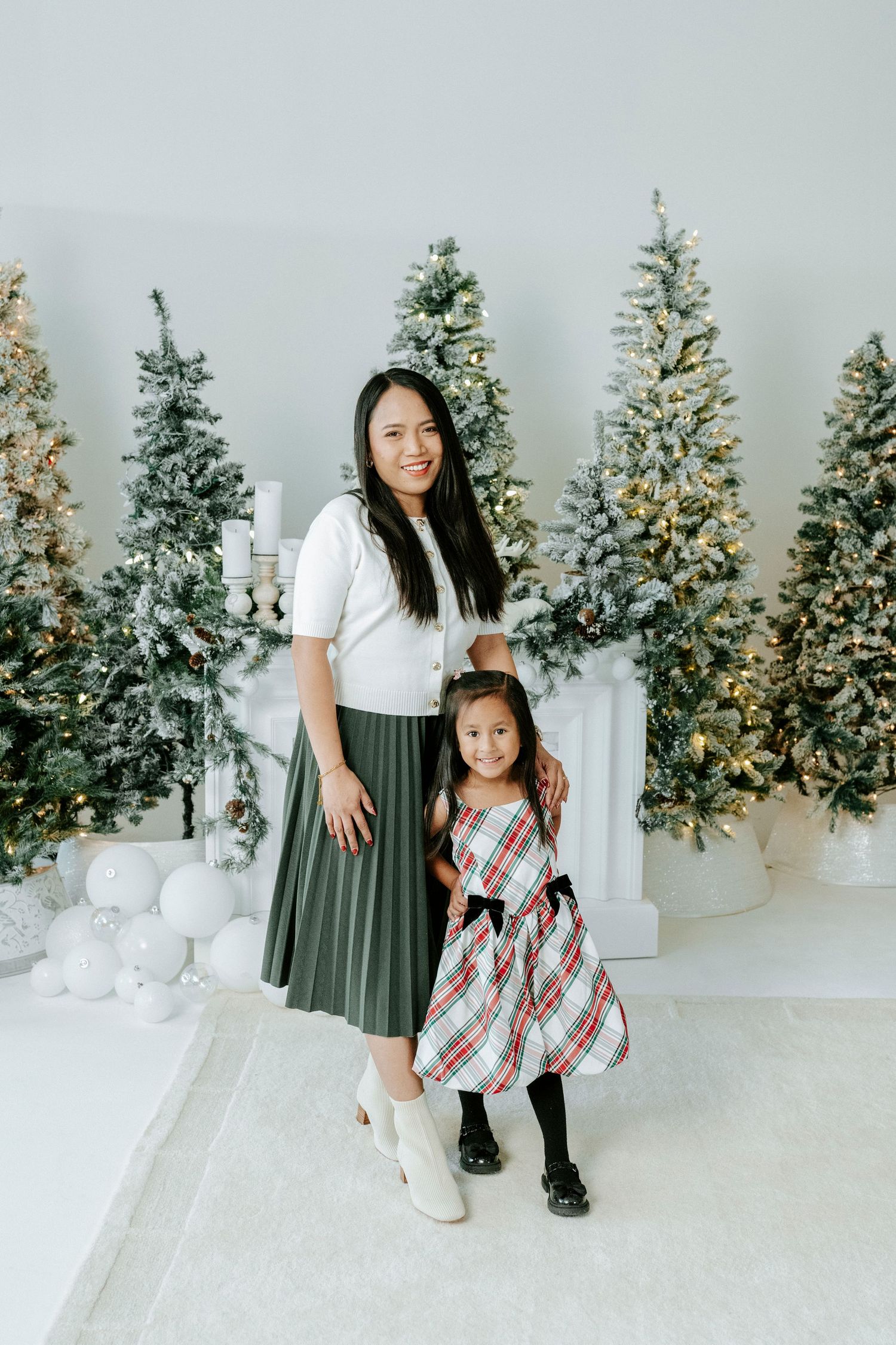 A festive holiday photoshoot scene with decorated Christmas trees, white presents, and matching plaid outfits.