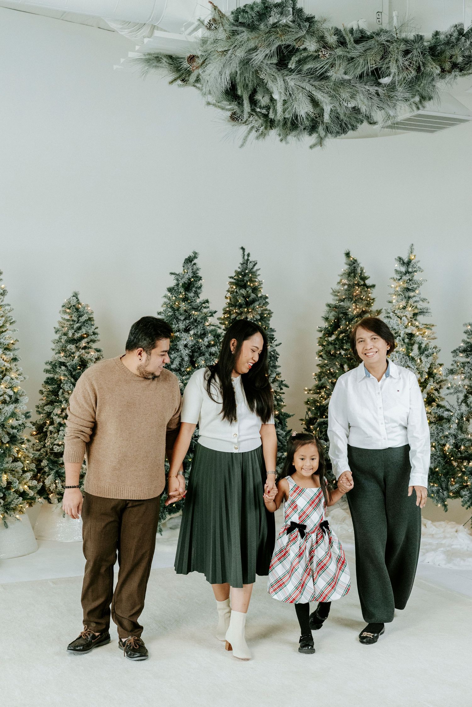 A family in coordinated brown and white outfits poses together against a winter wonderland backdrop with Christmas trees.