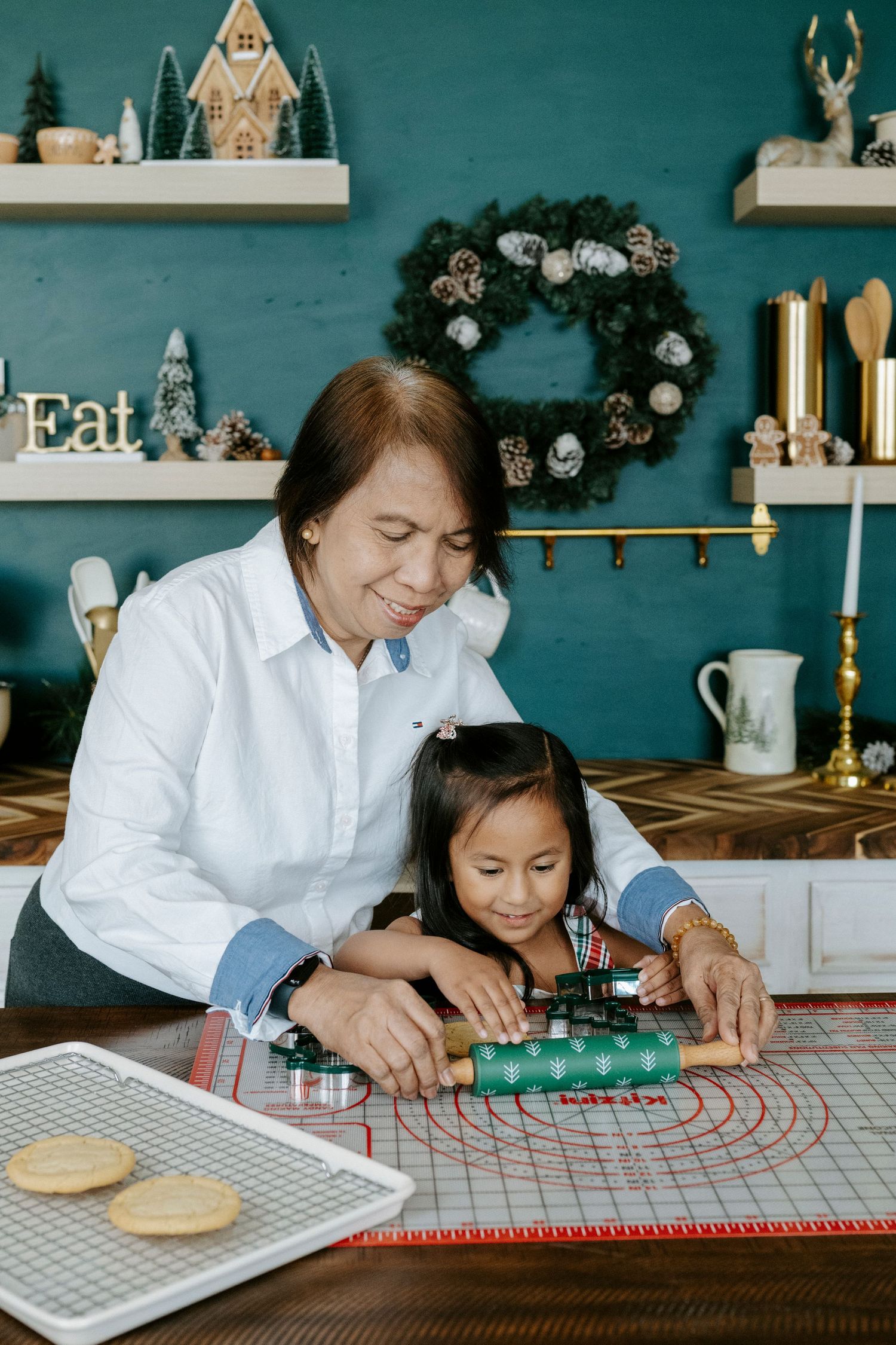 Two people work together to create patterns on a wooden surface with red string in a cozy kitchen setting.