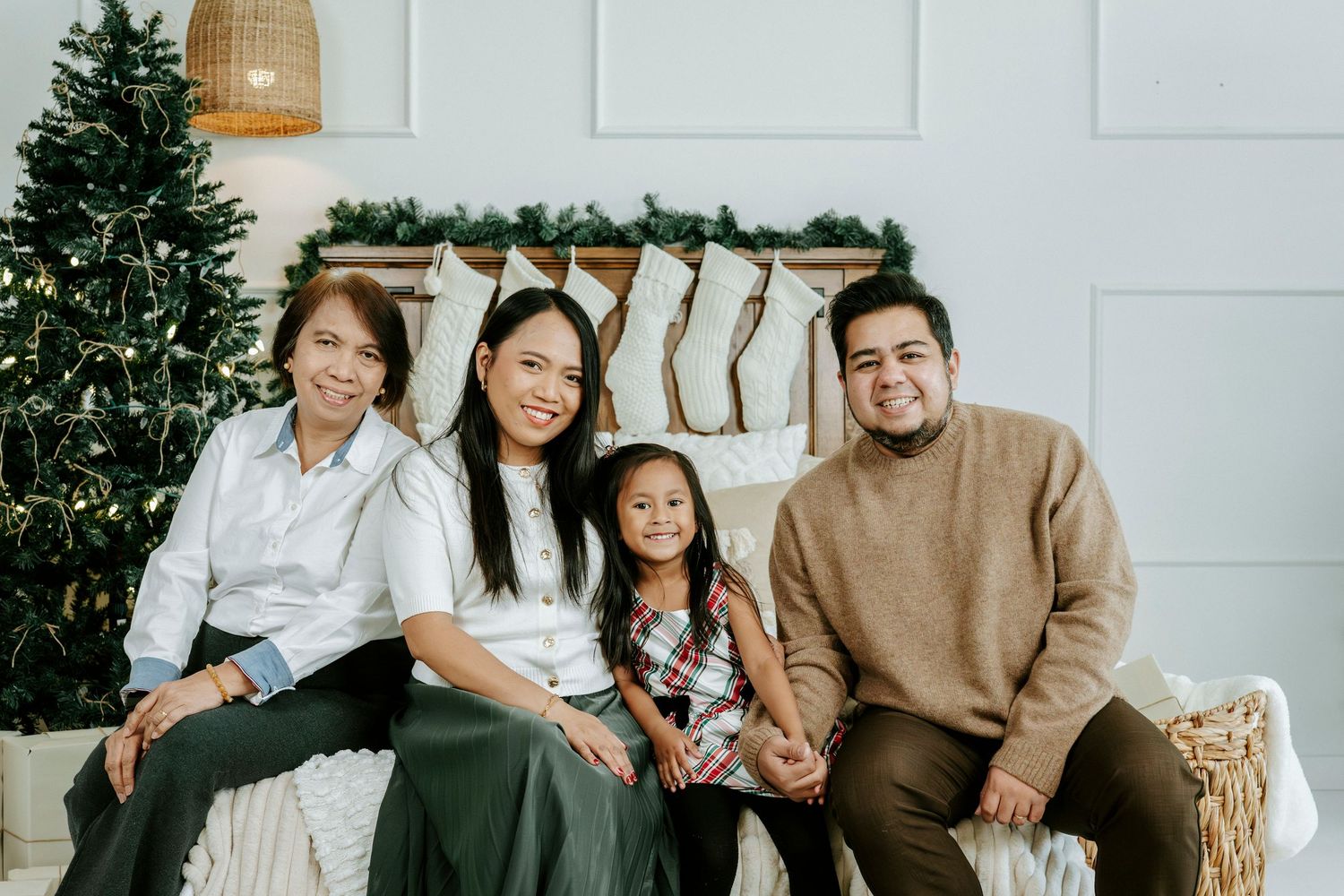 A family sits together on a couch during the holiday season with a Christmas tree and stockings in the background.