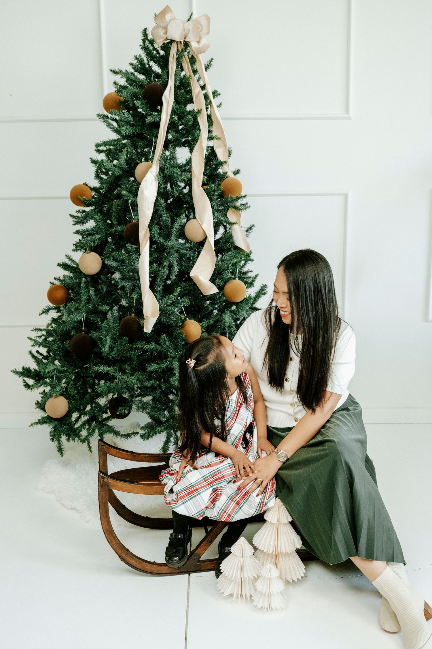 Christmas tree decorated with ornaments and ribbons in a minimalist white room setting.