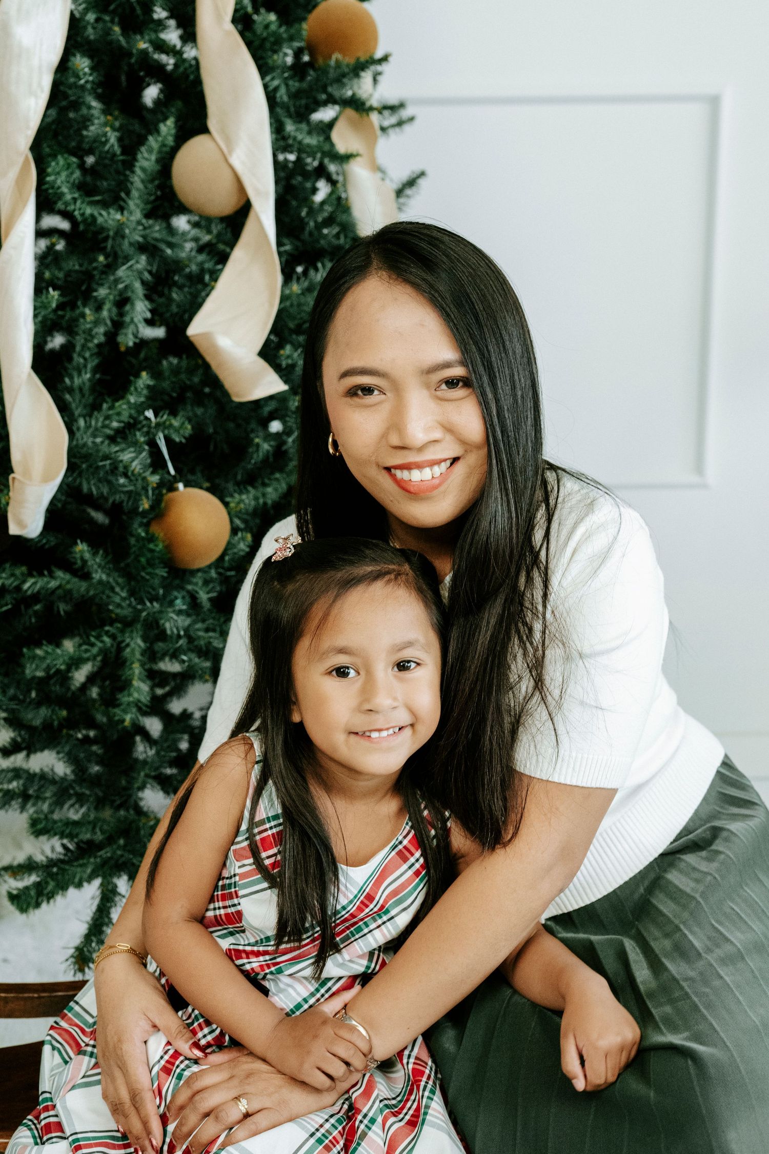 A joyful holiday portrait session with matching plaid dresses against a Christmas tree backdrop.