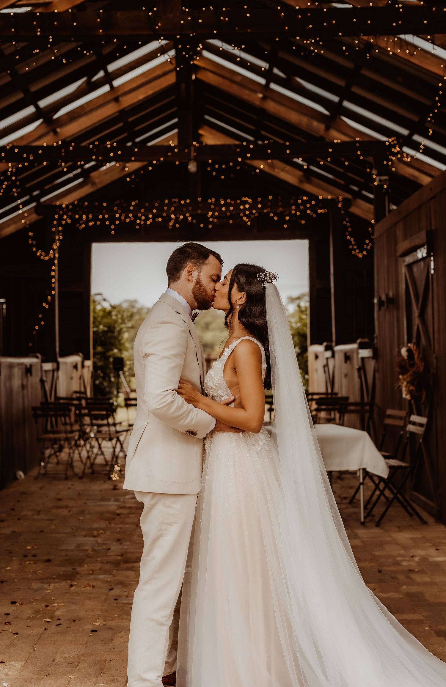 A romantic moment captured in a rustic barn venue decorated with twinkling string lights.