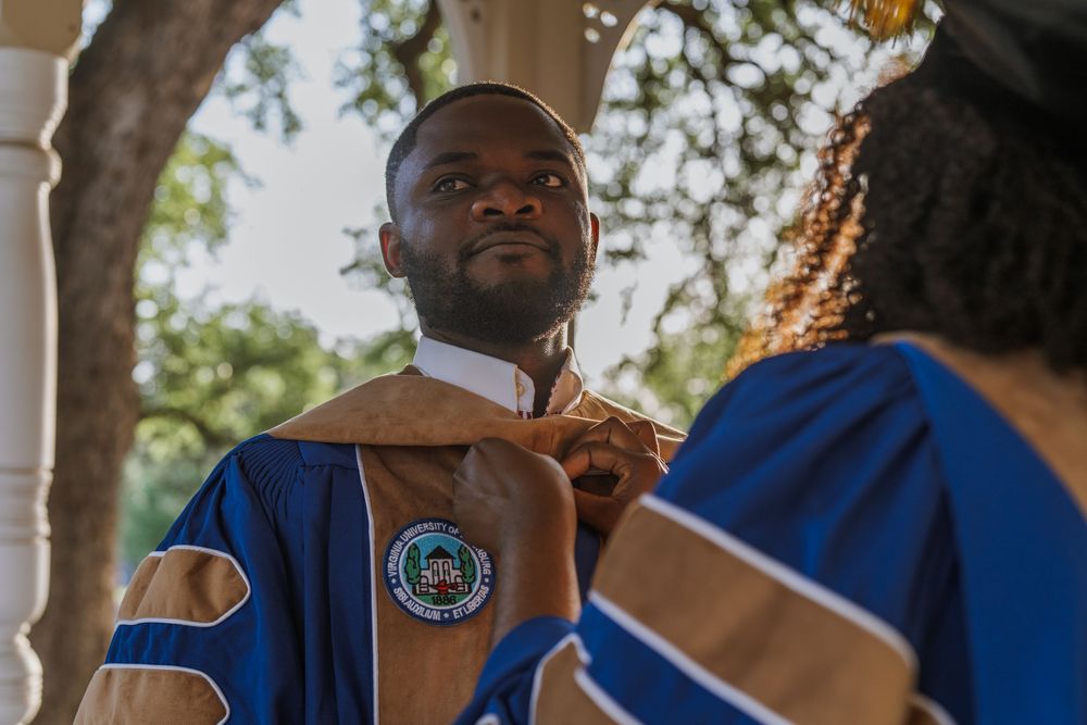 Graduates in blue and white regalia gather during outdoor commencement ceremony.