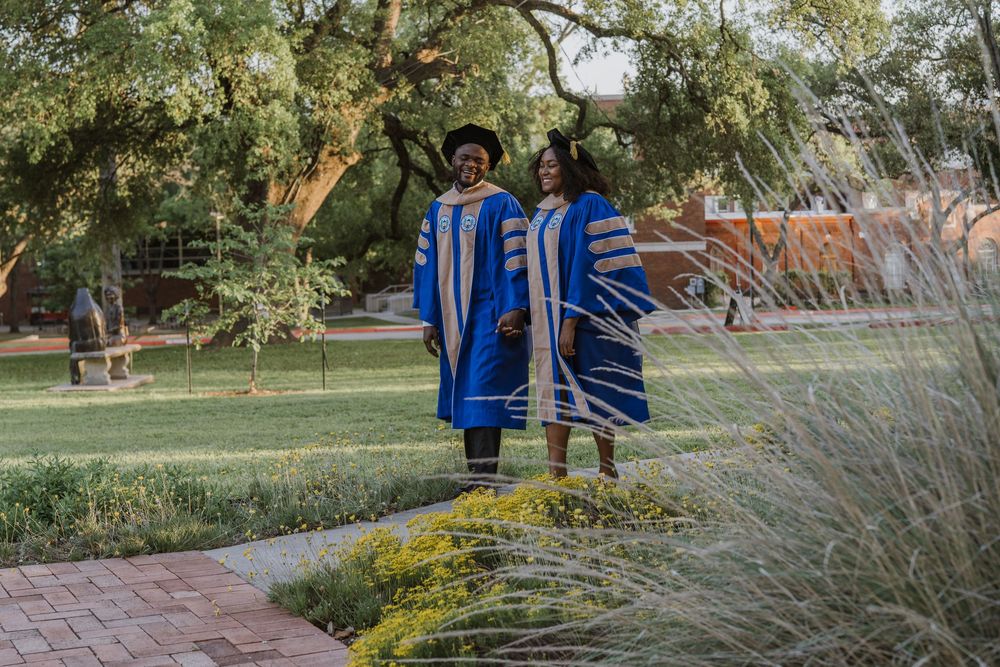 Graduates in blue and gold academic regalia walking through landscaped garden path.