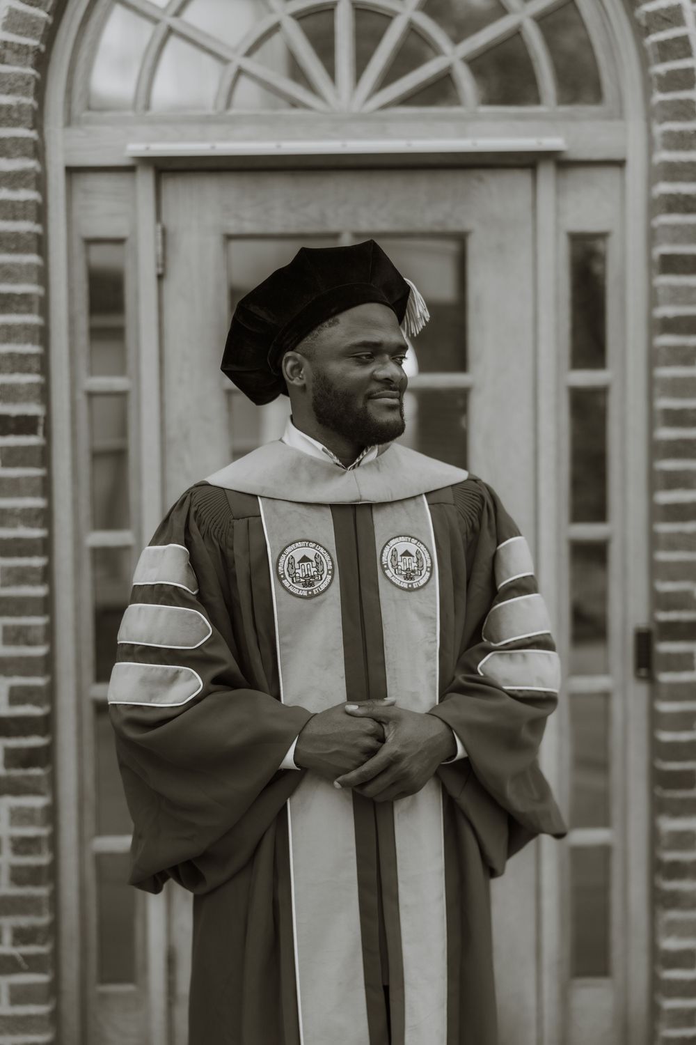 Black and white photo of graduates in academic regalia standing before arched doorway.