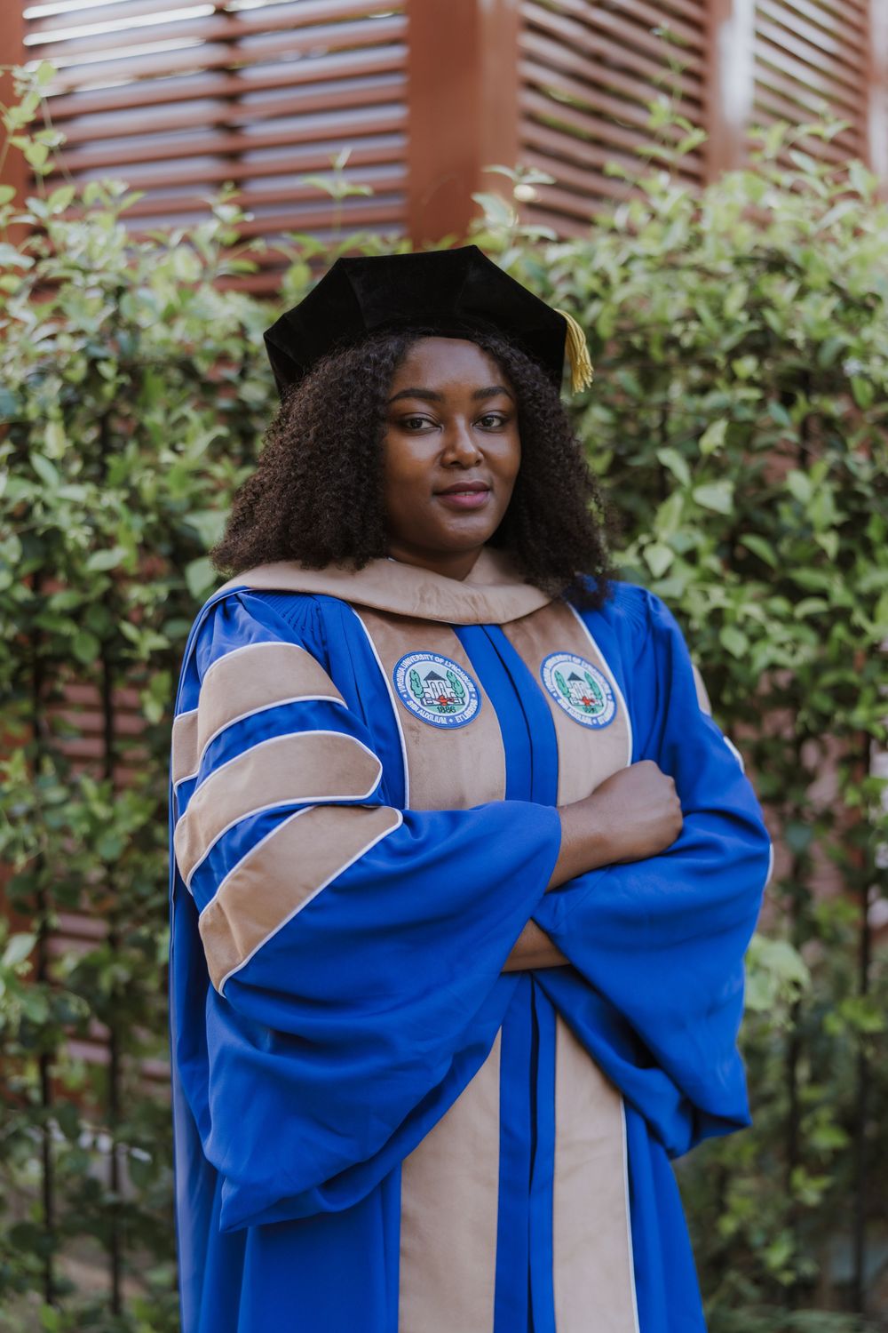 Graduate in blue academic regalia with gold stole poses outdoors.