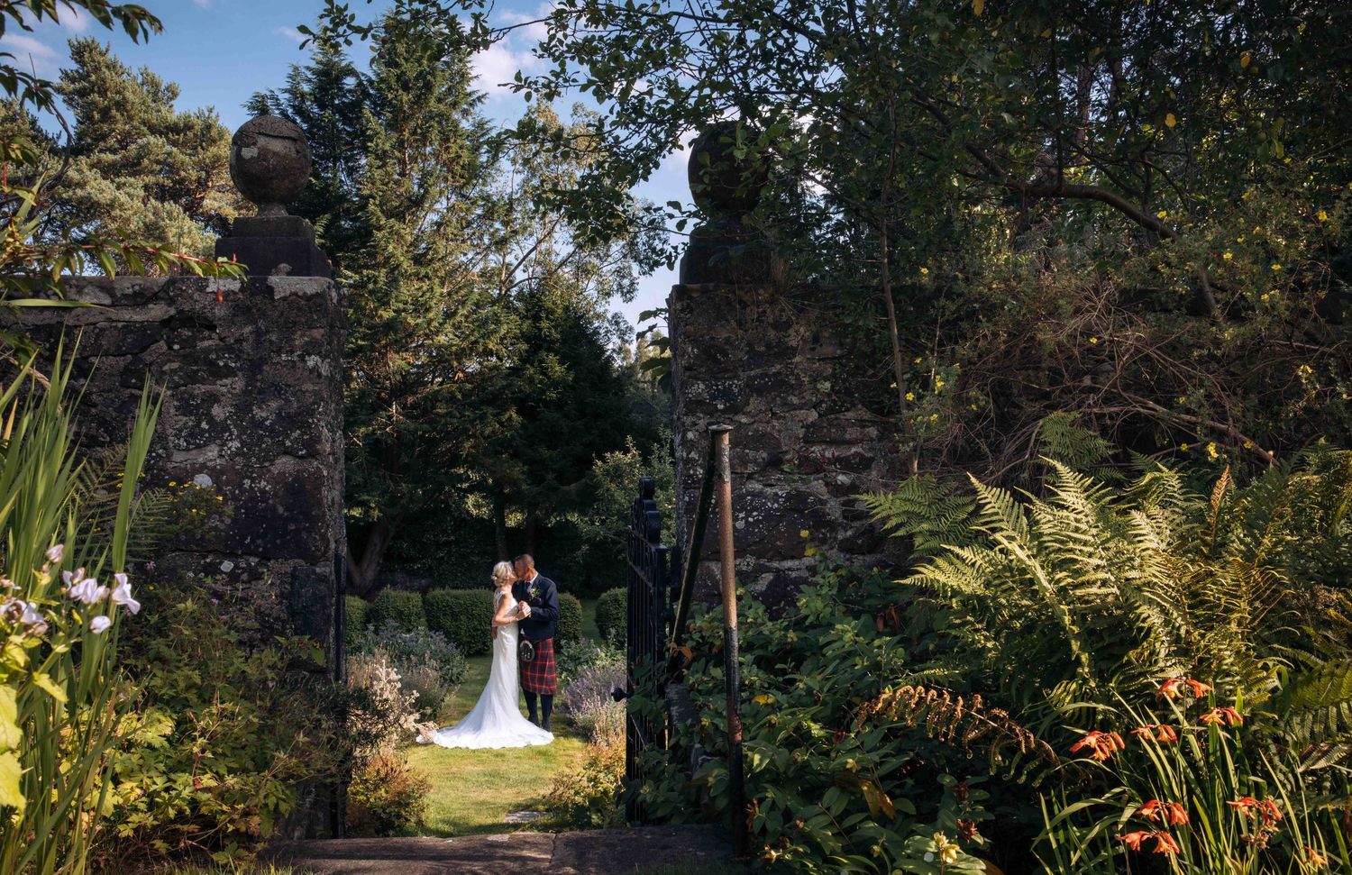 A scenic outdoor wedding ceremony setup with white chairs arranged in rows under tall evergreen trees.