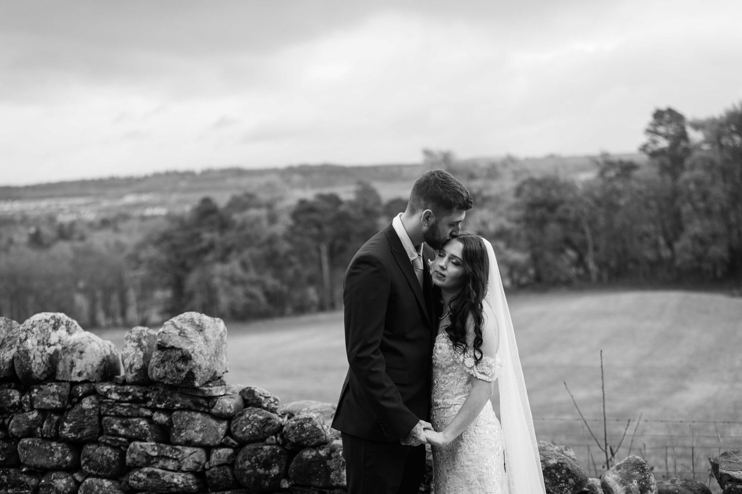 Black and white wedding photographs arranged in a panoramic collage showing romantic moments in a countryside setting.