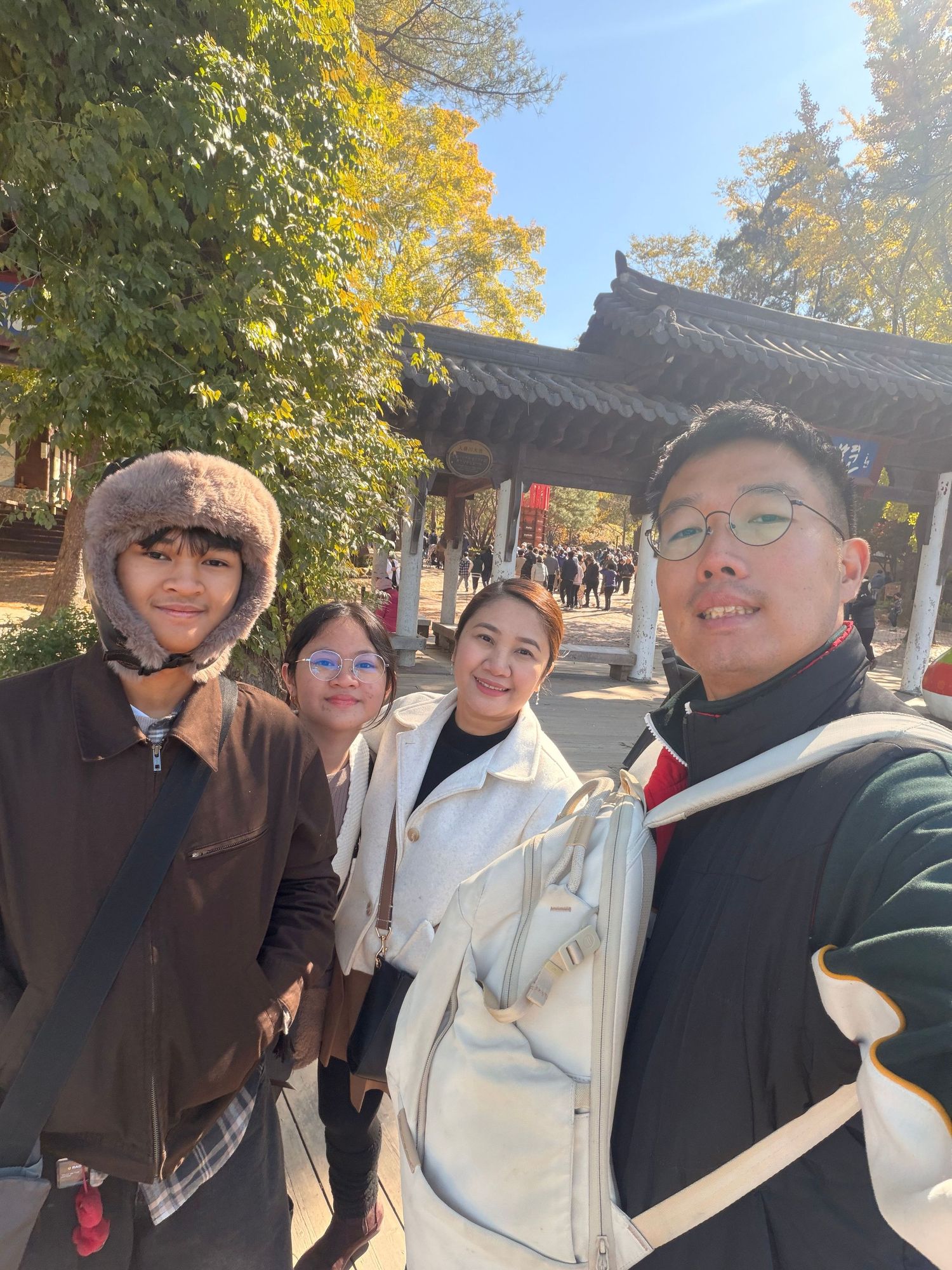 A group of friends enjoying autumn weather outdoors with yellow leaves visible in the trees behind them.