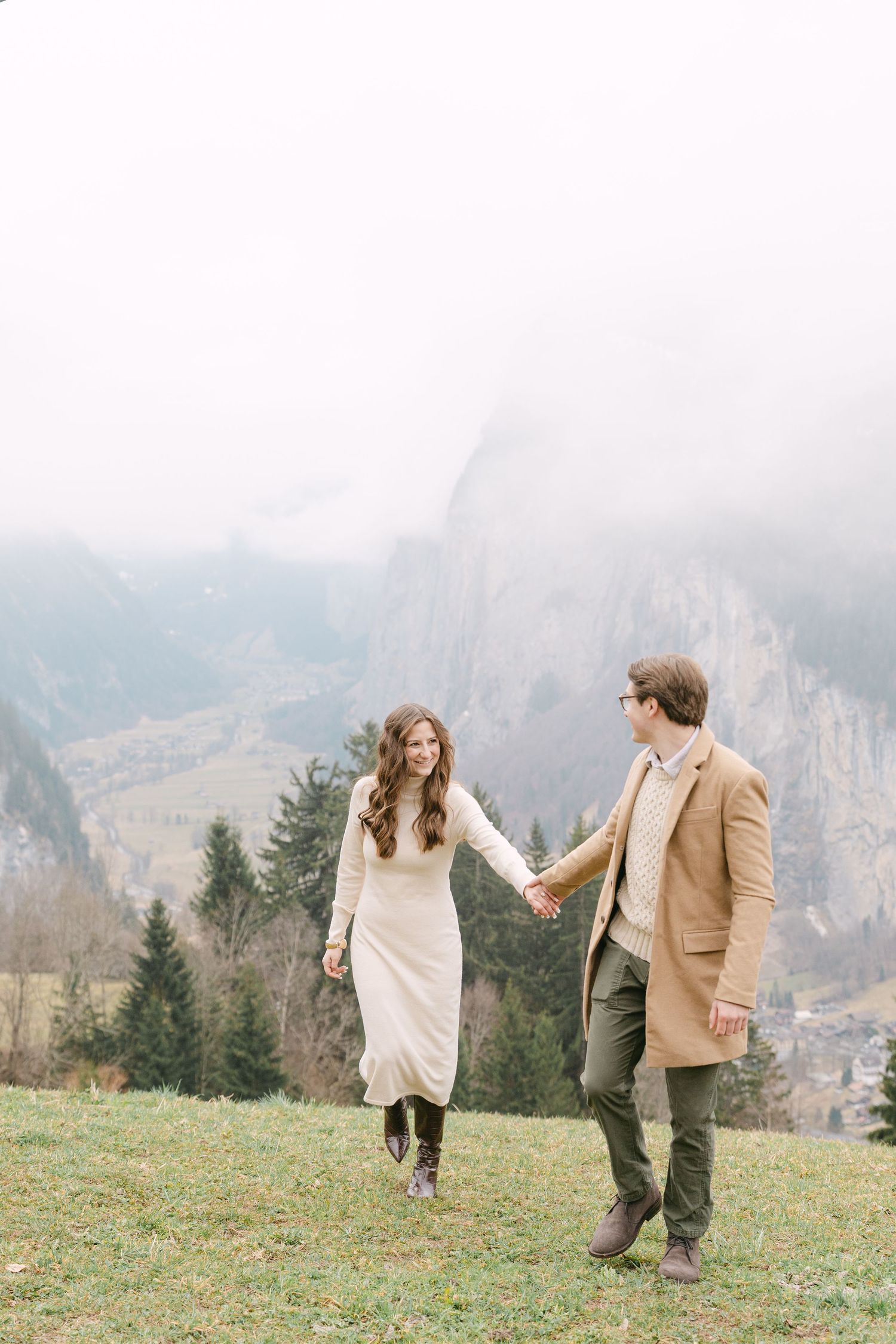 A couple shares a romantic moment while walking through a misty mountain meadow in the Alps.