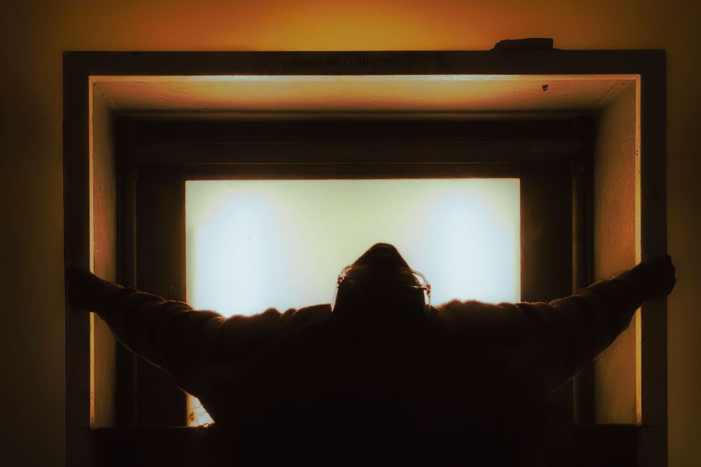 Silhouetted figures against backlit window frames in warm tones.