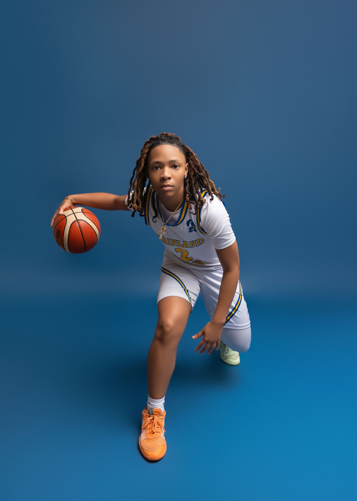 Basketball player in white uniform dribbles ball in dynamic sequence showing four different motion poses against blue background.