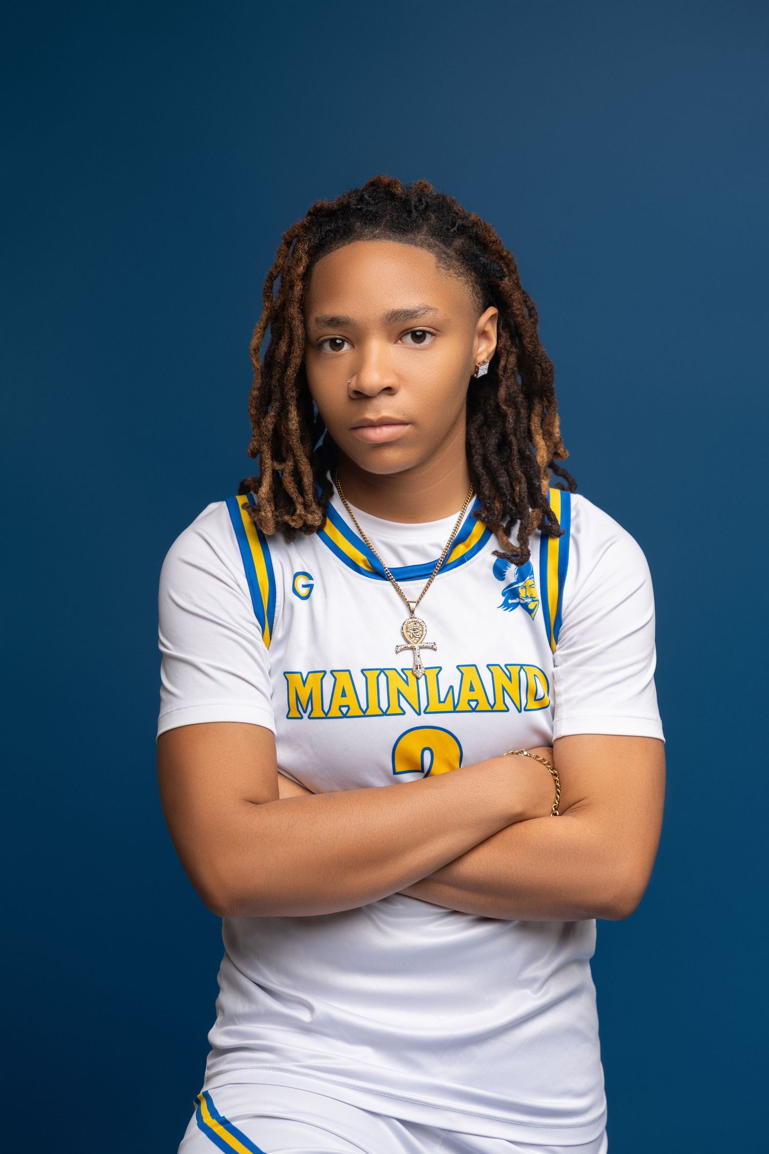 High school athlete poses in white Mainland sports uniform against dark blue background for team photos.