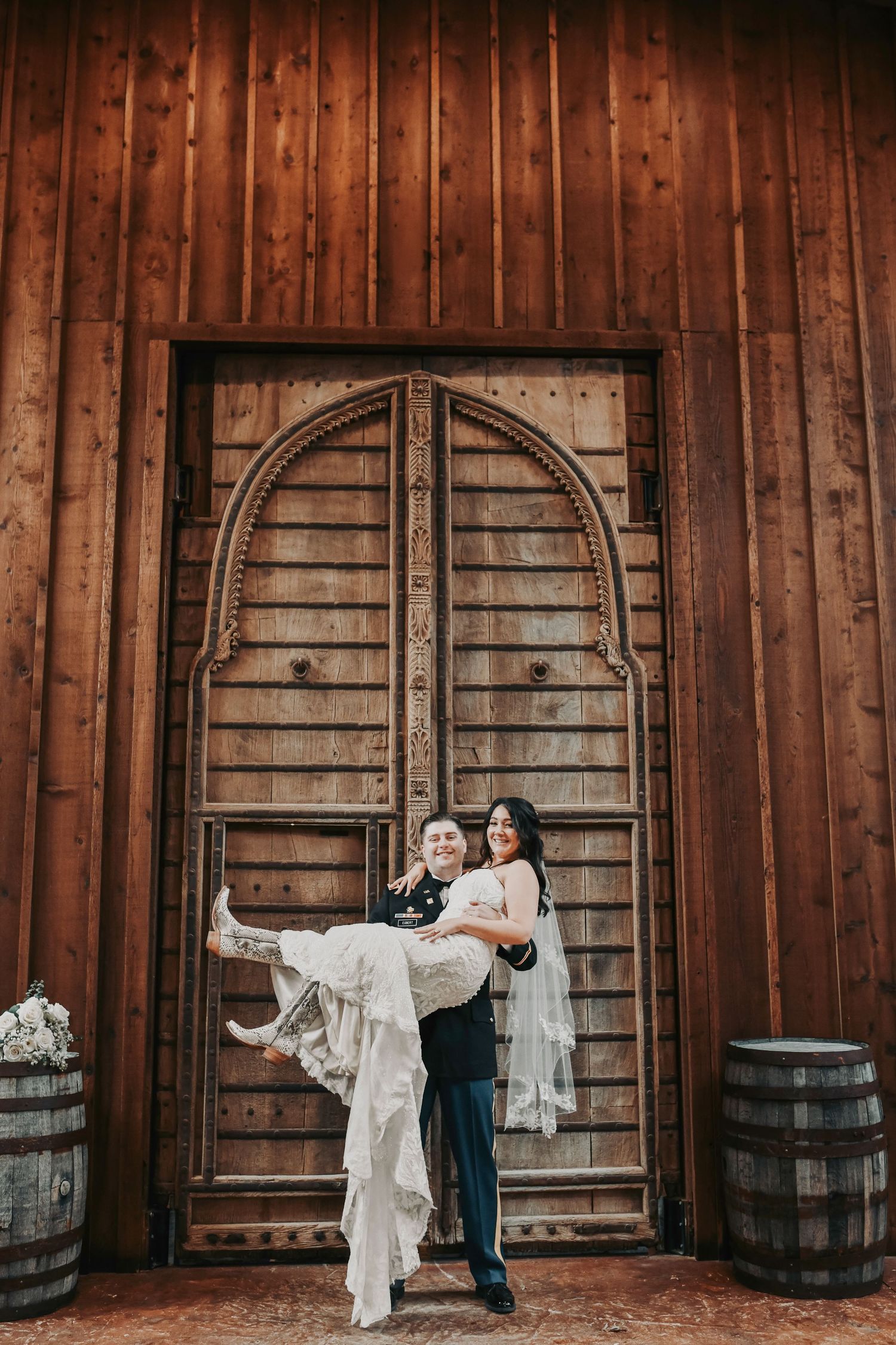 Bride and groom sharing a kiss in front of sweeping wooden doors at their elegant ranch wedding.