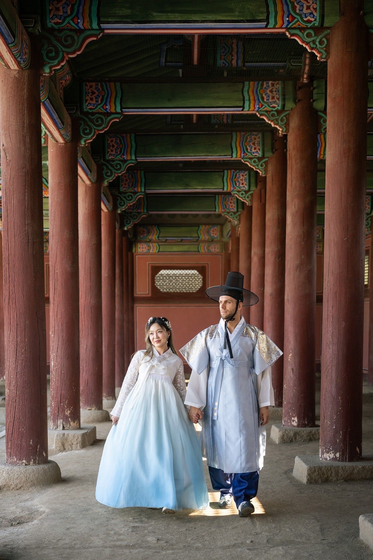 Traditional Korean hanbok-wearing visitors walk through the ornate wooden pillars of Gyeongbokgung Palace in Seoul.