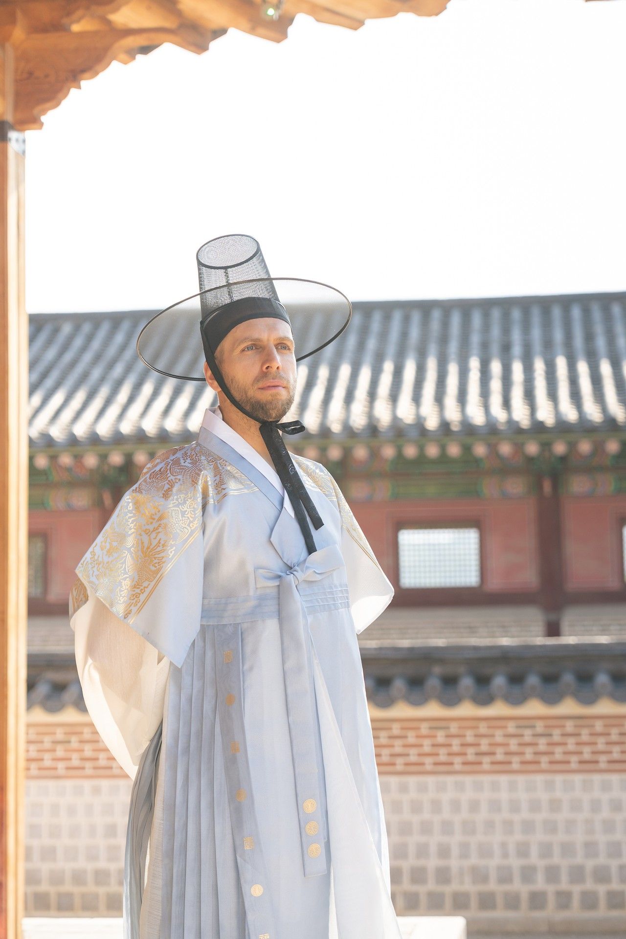 Figure in traditional Korean hanbok attire stands in front of historic palace wall during sunny day.