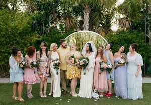 Wedding party in pastel dresses standing together outdoors in a garden setting.