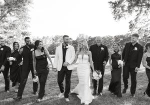 Wedding party walking in a line across a grassy field in black and white photography.