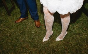 Close-up of formal shoes and dress hems on grass at outdoor wedding.