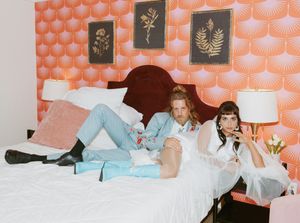 Wedding party lounging on a bed with peach-colored wallpaper in a relaxed candid moment.