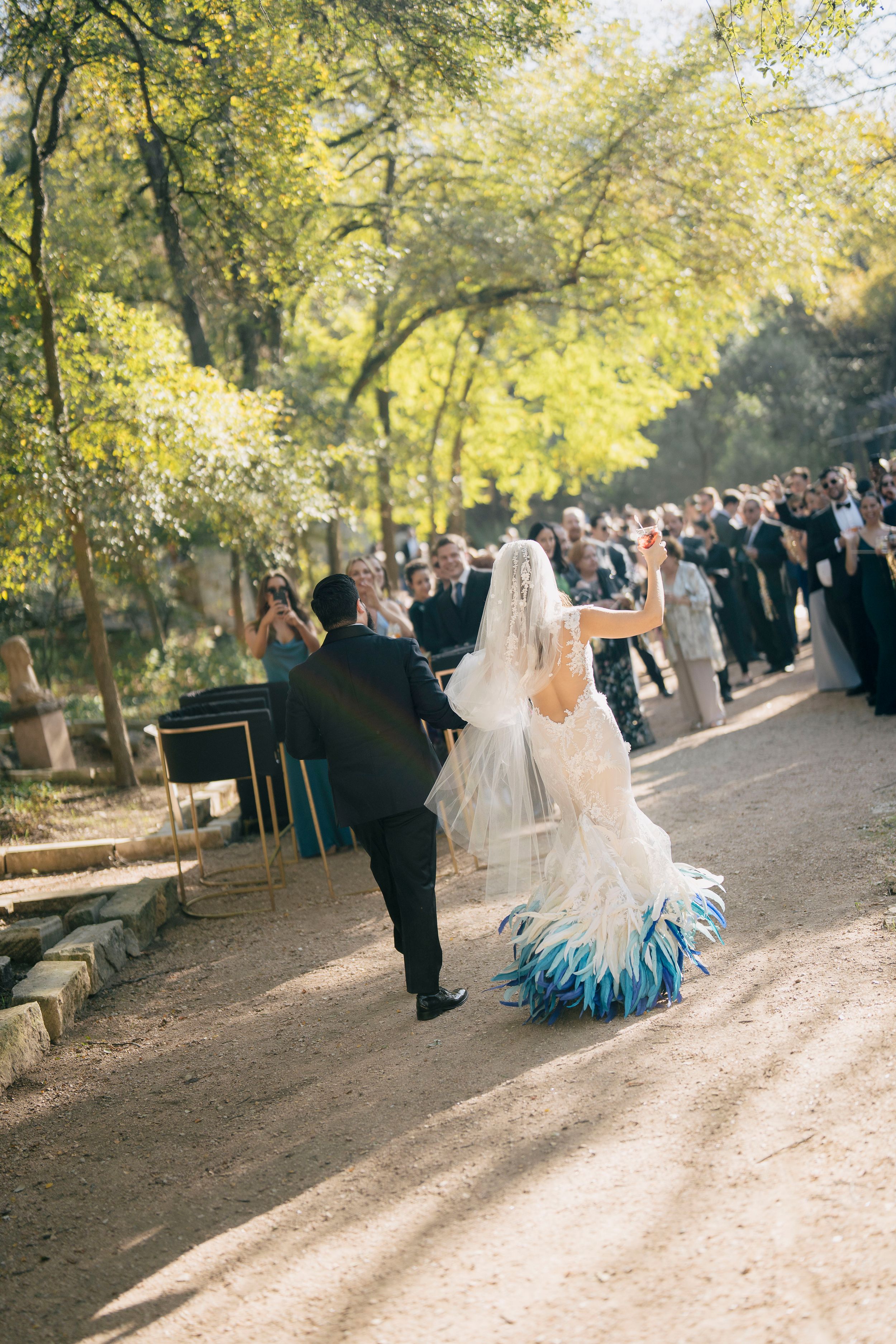Wedding couple dancing along a tree-lined path as guests look on during an outdoor autumn destination wedding celebration.