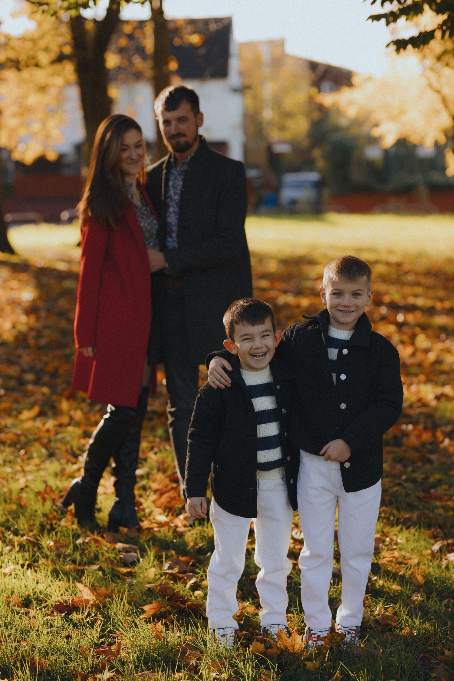 A family walks together through fallen autumn leaves in a park during golden hour sunset.