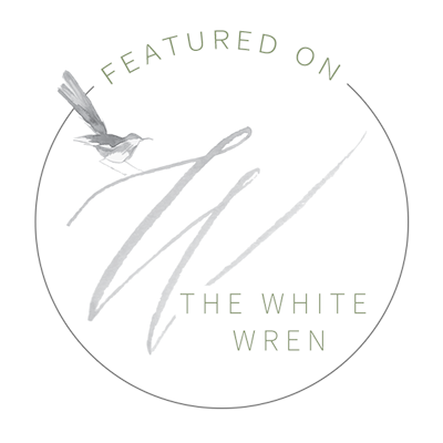 A minimalist circular logo design featuring a small bird silhouette and text reading 'THE WHITE WREN' in gray tones.