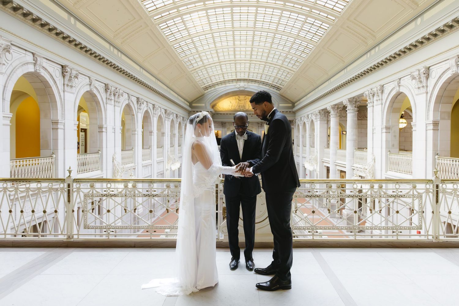 A panoramic view of a grand white marble corridor with ornate columns and arched glass ceiling in a historic building.
