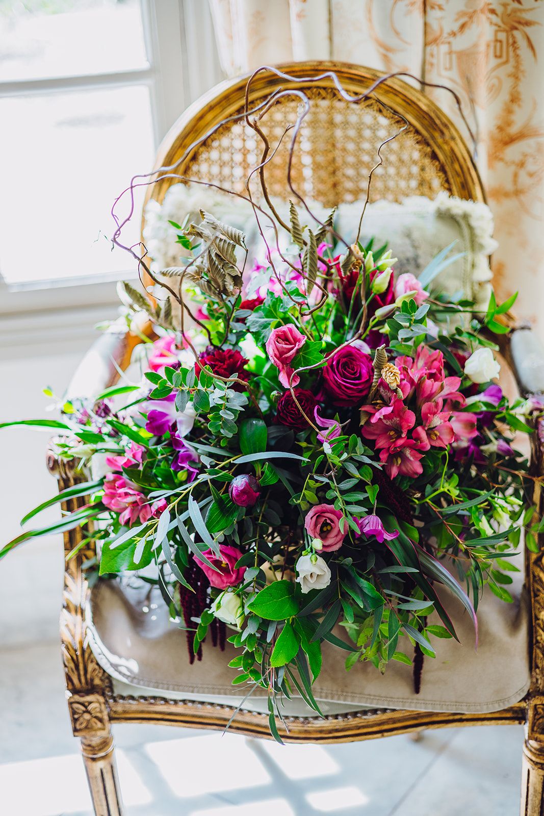 Elegant floral arrangement with pink roses and purple blooms in vintage gold frame settings against white interior decor.