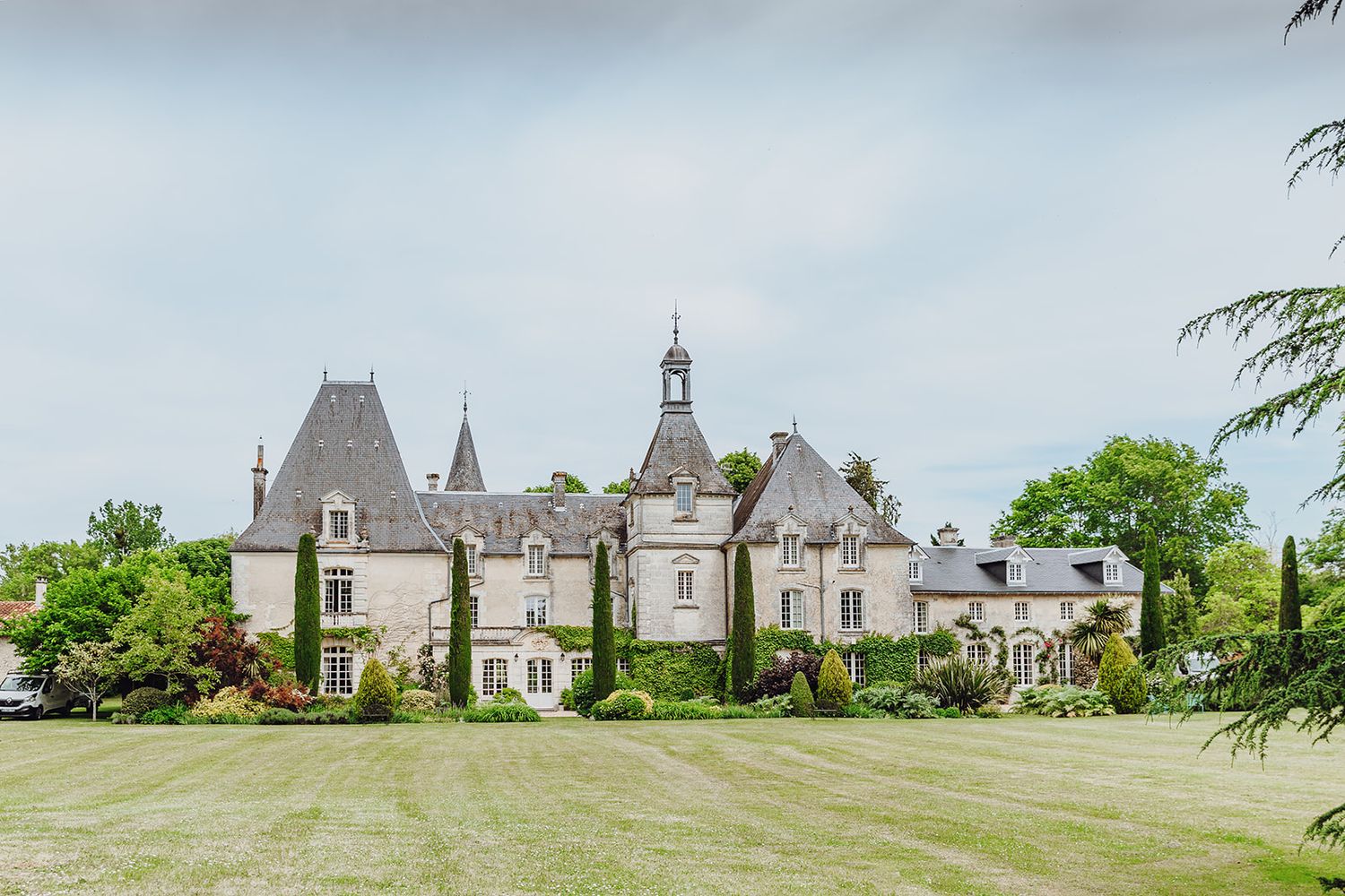 A panoramic view of a historic French chateau with multiple spires and towers set against a green landscape.