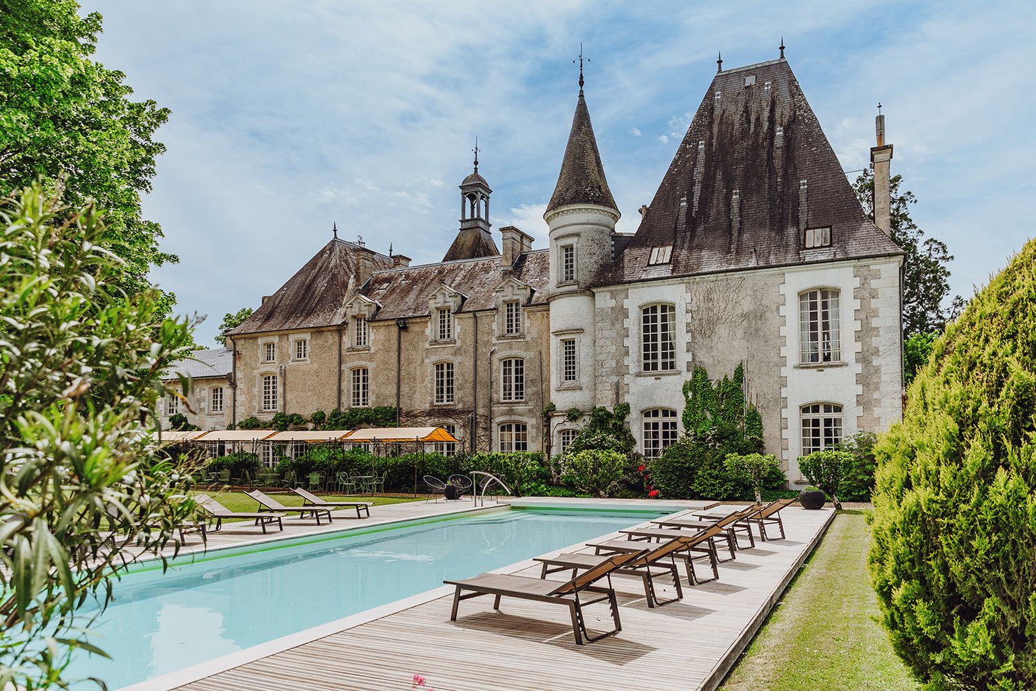 Luxury French chateau estate with swimming pool and lounge chairs surrounded by manicured gardens and historic architecture.