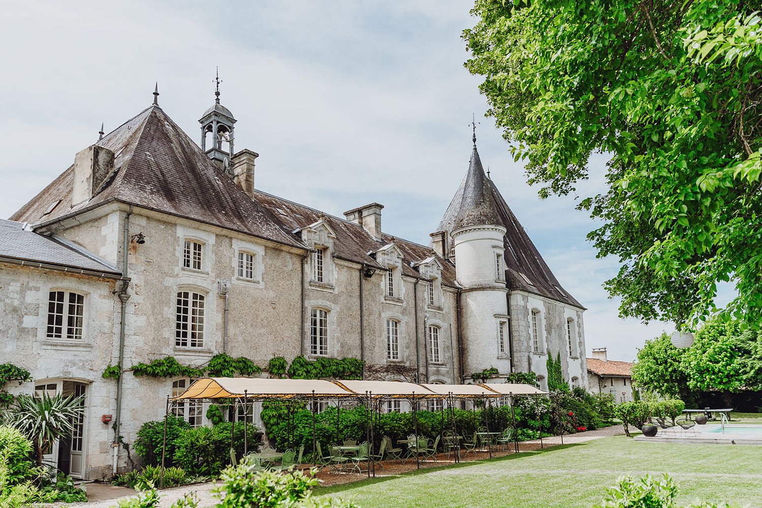 A panoramic view of a historic French chateau with multiple buildings and lush green gardens in summer.