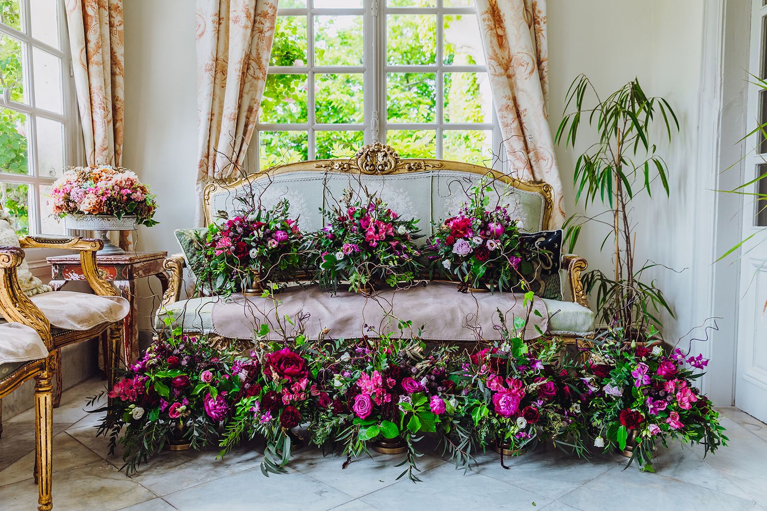 Bright sunroom with wicker furniture and vibrant pink flowers decorating the windowsills and corners.