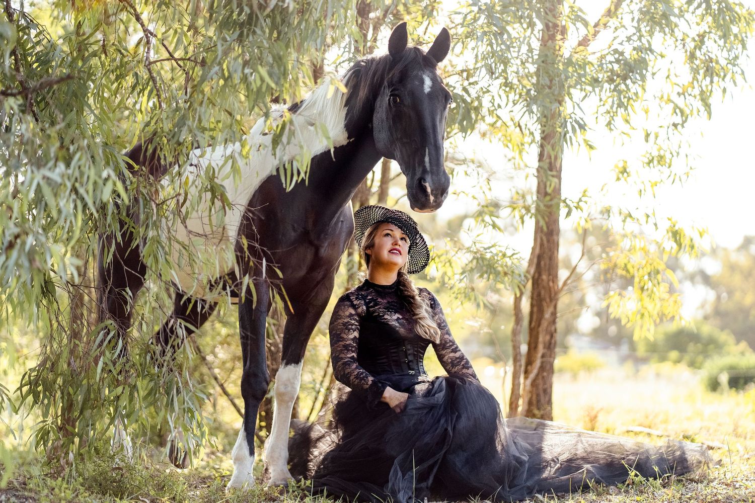 A black and white horse stands to rest under a shady tree on a sunny afternoon with a lady during a horse photoshoot in Sydney