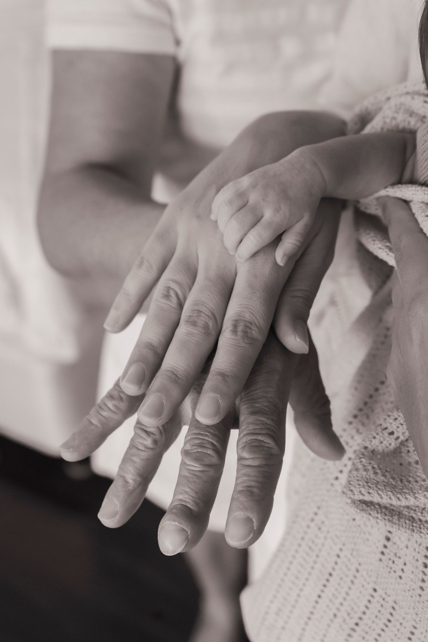 Newborn photography session. Detailed black and white photograph of hands resting on textured knit fabric.