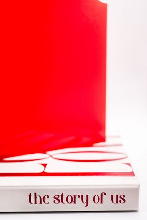 Red and white book titled 'The Story of Us' lying on a white surface with dramatic lighting and shadow.