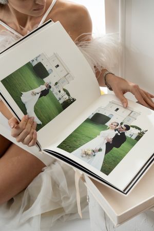Hands holding and flipping through pages of a white wedding photo album.