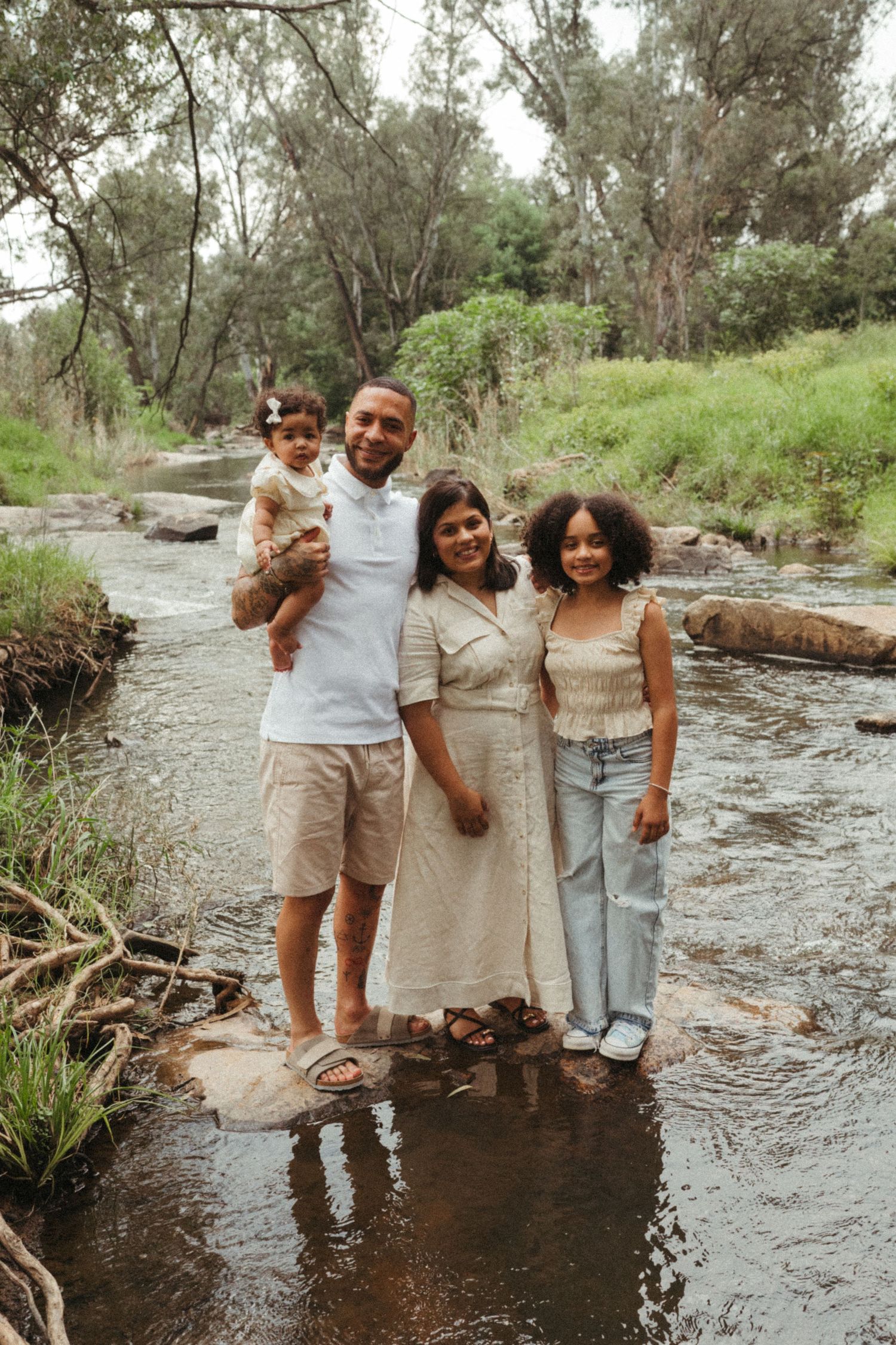 Family members standing in a stream during a casual outdoor photoshoot.