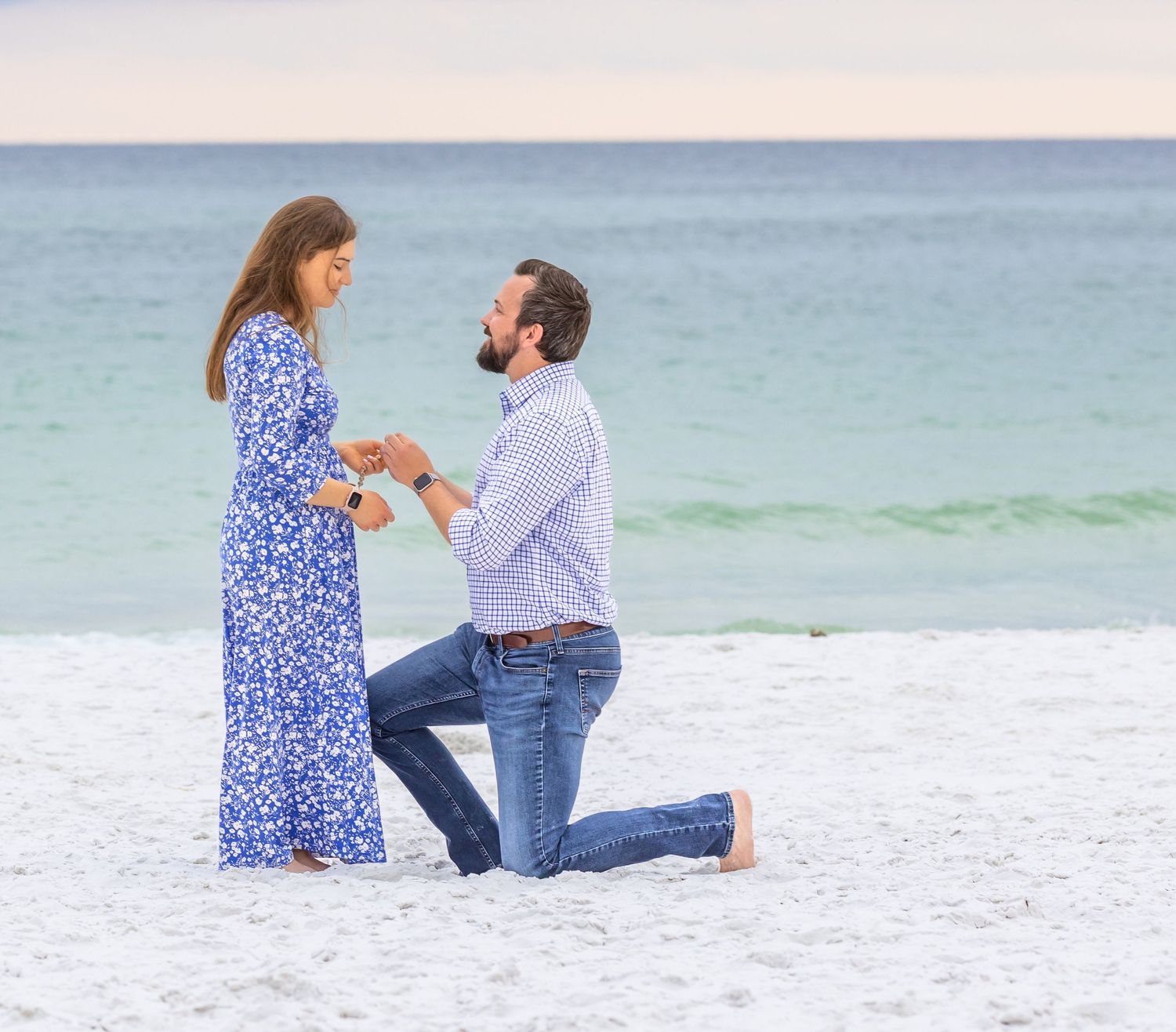 A couple shares a romantic moment on a white sandy beach with turquoise waters in the background.