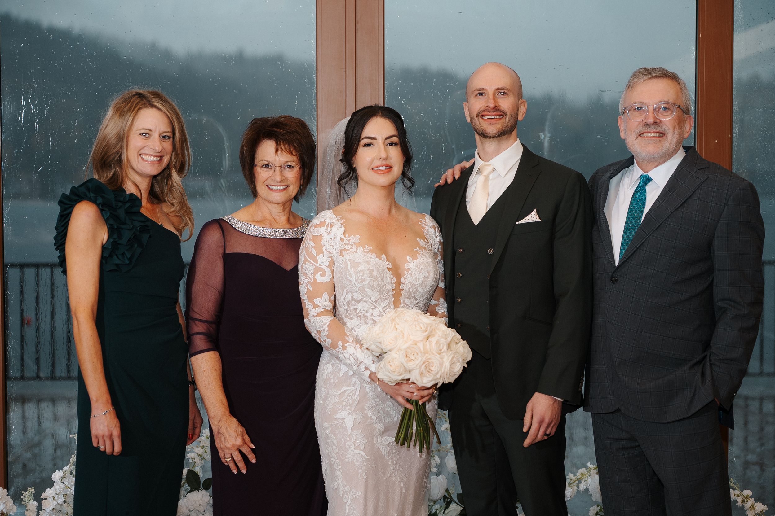A group of five people in formal attire pose together at a scenic mountain overlook.