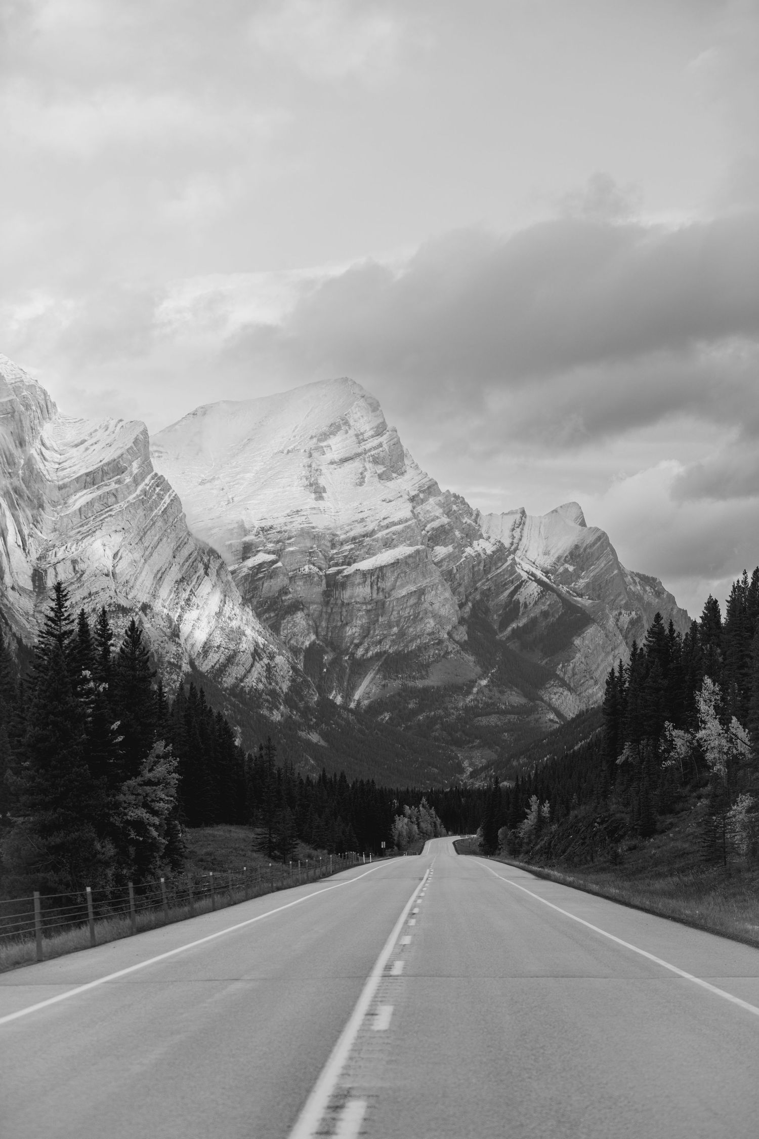 A scenic mountain highway winds through snow-capped peaks in Banff National Park on a cloudy winter day.