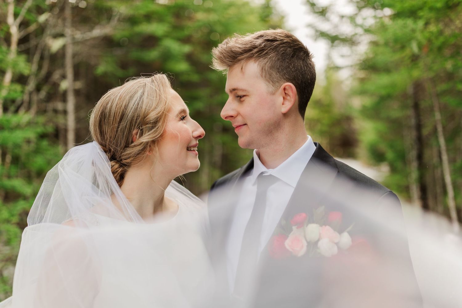 A couple in wedding attire shares a romantic moment in a sunlit forest setting.