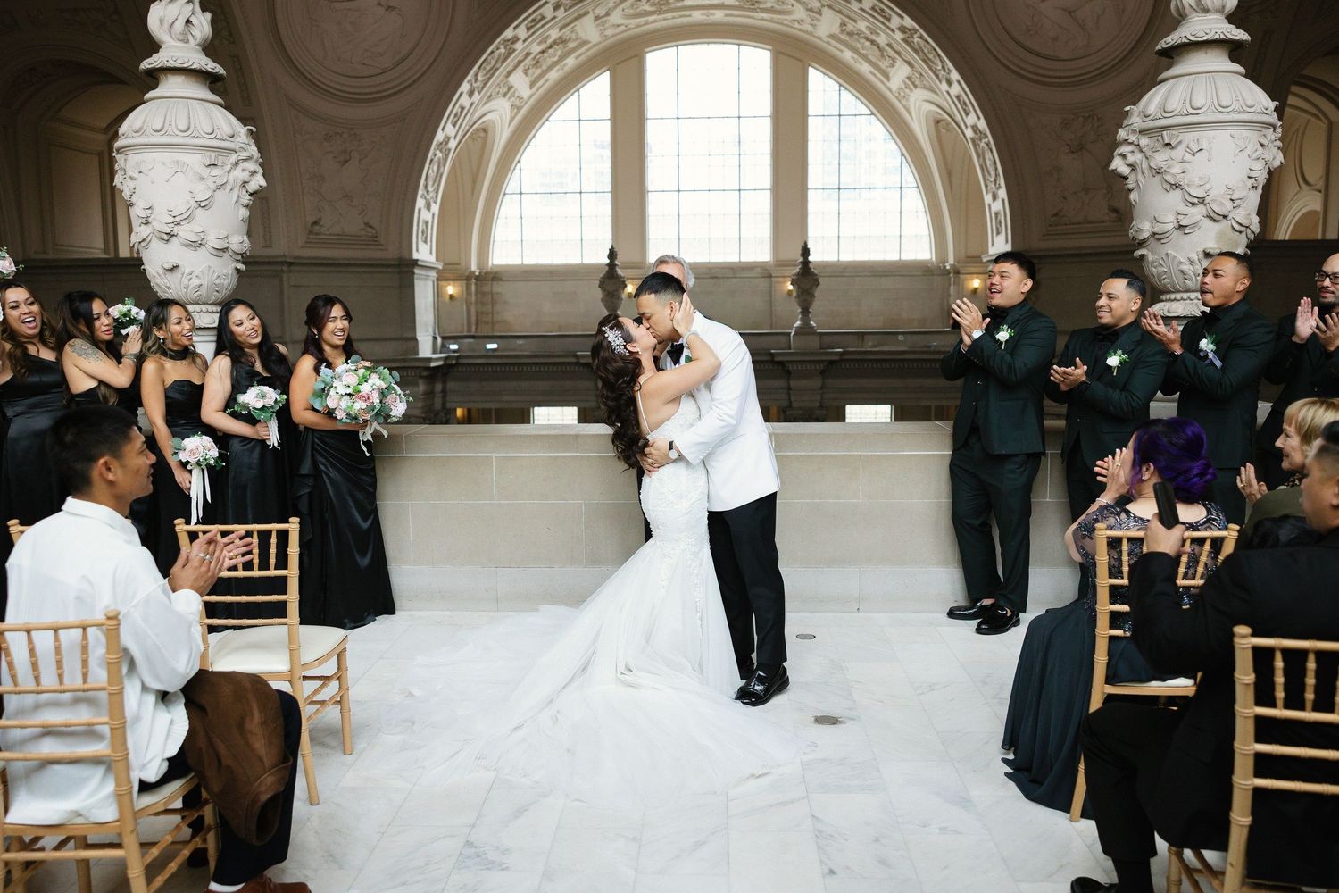Wedding party celebrates outdoors at a rustic venue with Spanish-style architecture and lush greenery.
