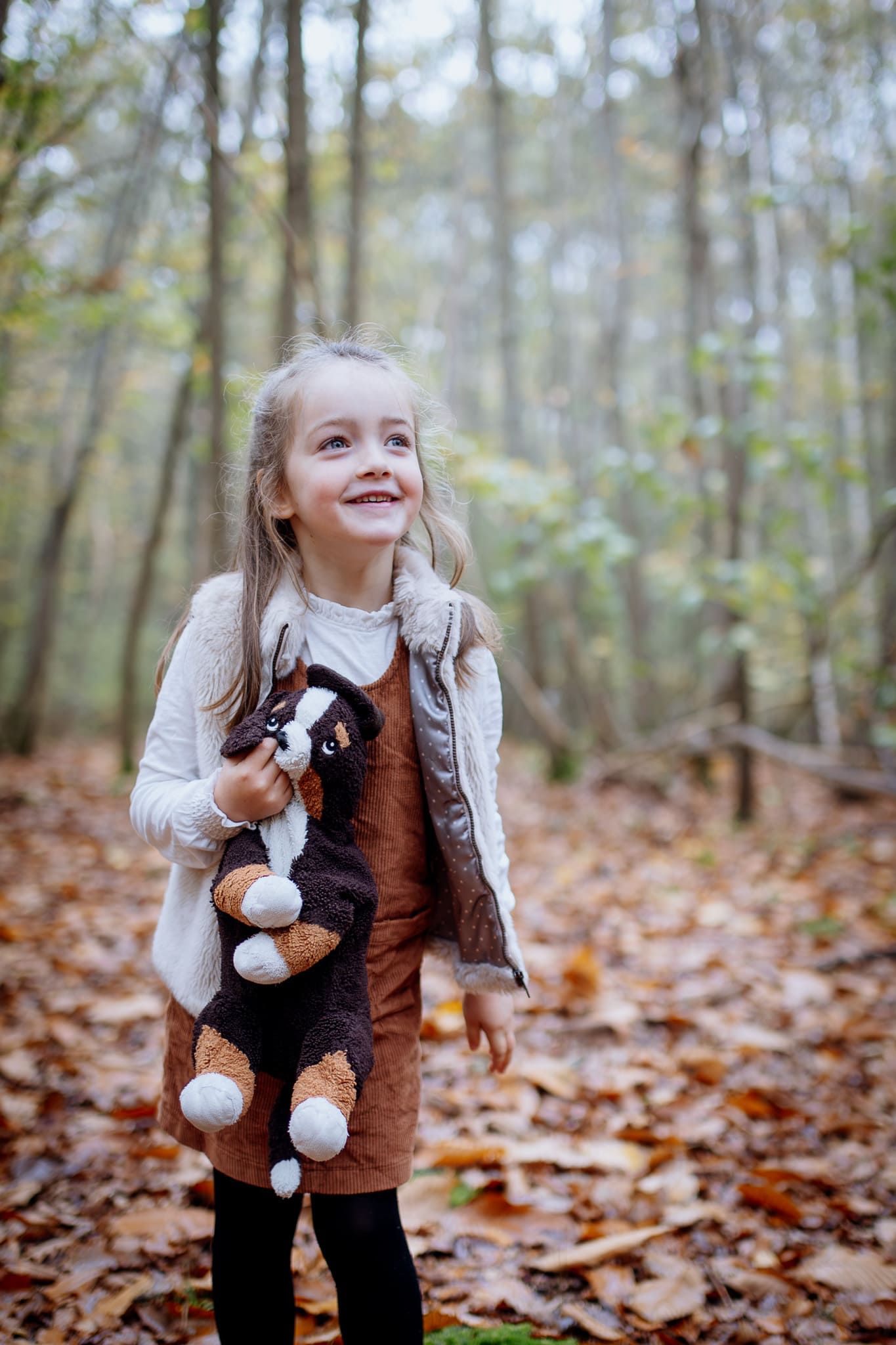 Petite fille qui sourit avec son doudou dans les mains dans la forêt de Behoust, yvelines