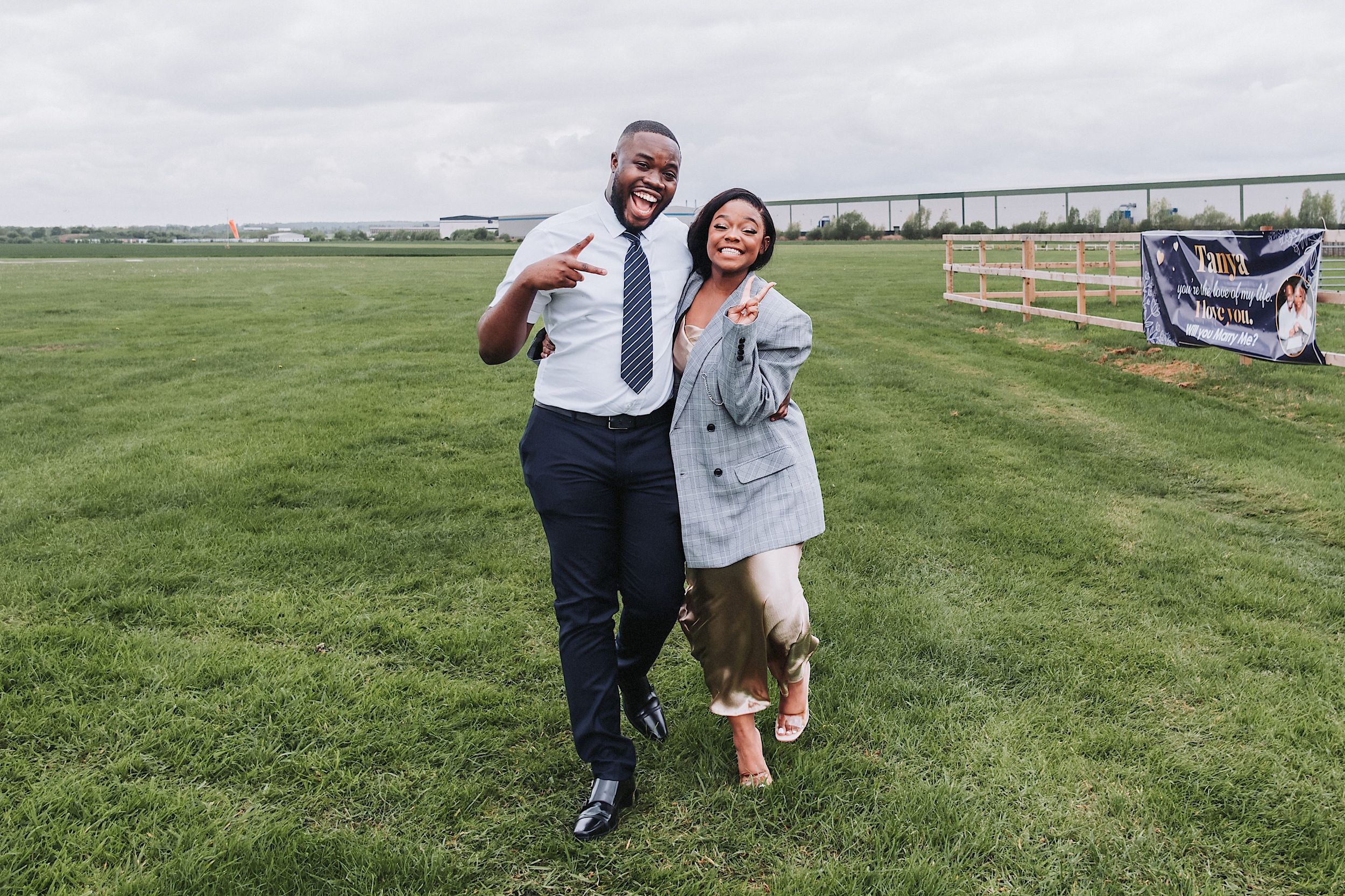 A couple laughs joyfully together while posing on a green grassy field during an outdoor photoshoot.