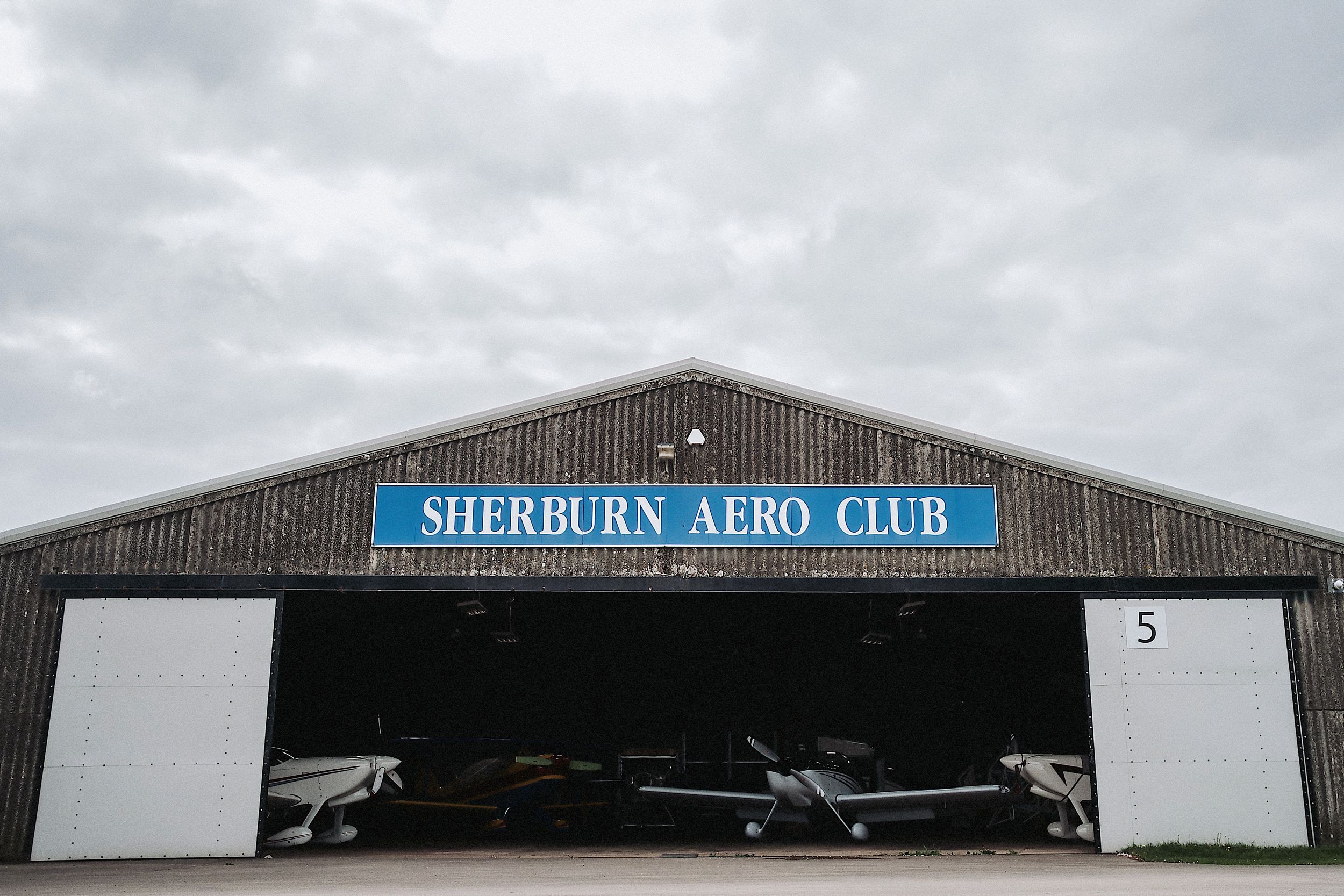 Panoramic view of an airfield with small aircraft parked in front of the Sherburn Aero Club building.